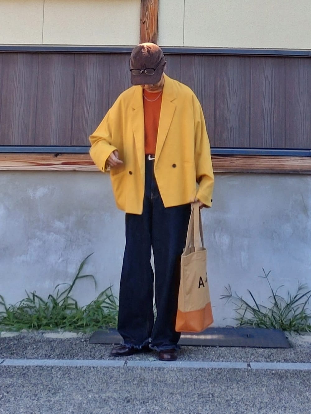 イエロー系のブルゾン、ブルー系のデニムパンツ、ブラウン系のトートバッグを着用したメンズの秋コーディネートの2枚目の写真