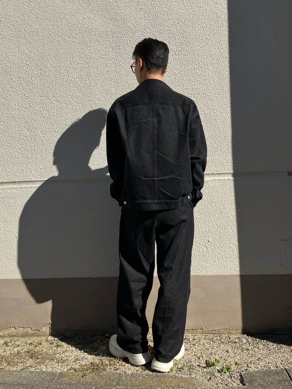 ブラック系のデニムジャケット、ブラック系のデニムパンツ、ホワイト系のスニーカーを着用したメンズの秋コーディネートの2枚目の写真