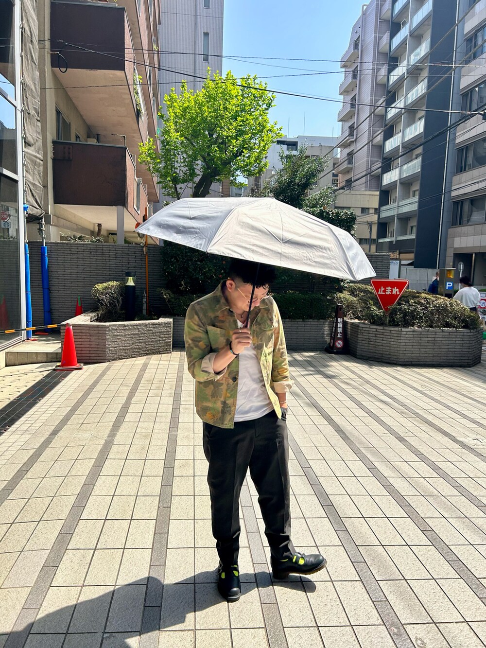 ブラック系のサンダル、グレー系のスラックス、ホワイト系の折りたたみ傘を着用したメンズの春コーディネートの2枚目の写真