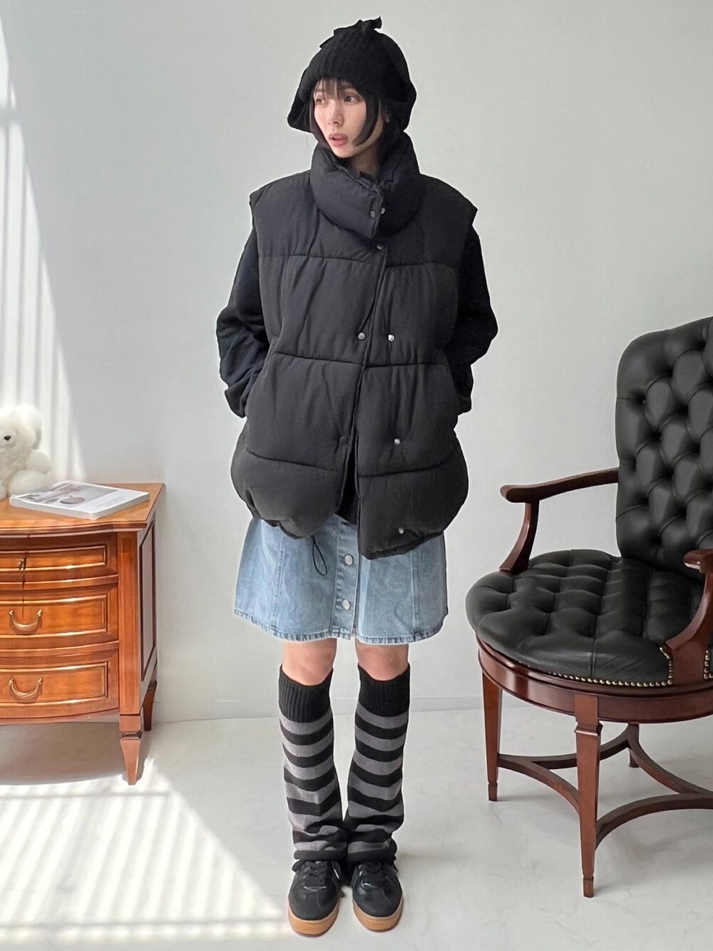 ブラック系のダウンベスト、ブルー系のデニムスカート、ブラック系のスニーカーを着用したレディースの秋コーディネートの2枚目の写真