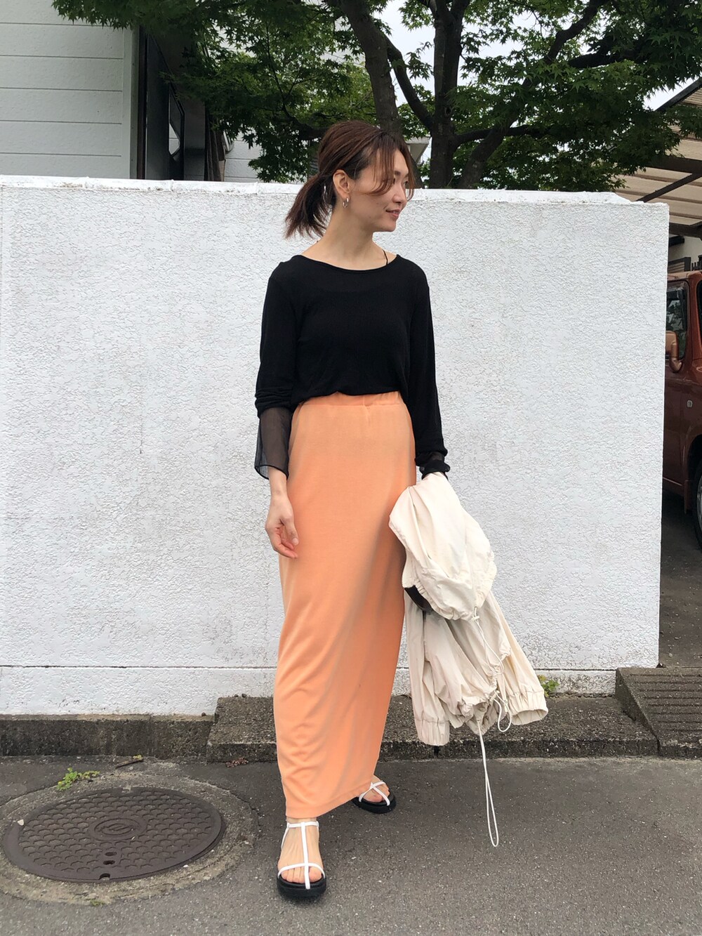 ブラック系のTシャツ/カットソー、オレンジ系のスカート、ホワイト系のサンダルを着用したレディースの夏コーディネートの2枚目の写真