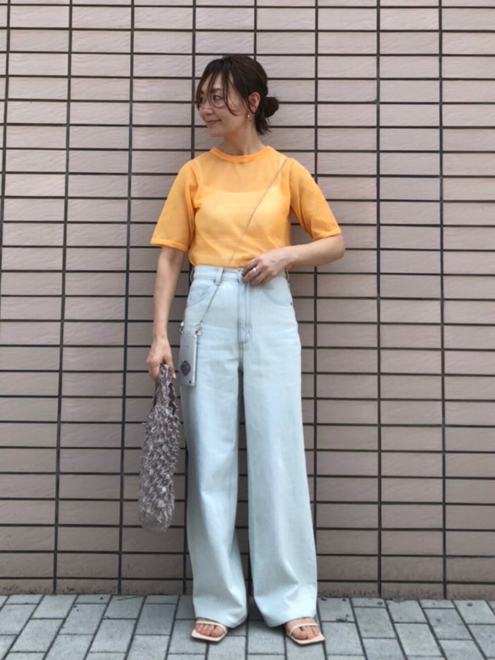 オレンジ系のニット/セーター、グレー系のエコバッグ/サブバッグ、その他のスマホケース/カバーを着用したレディースの夏コーディネートの4枚目の写真