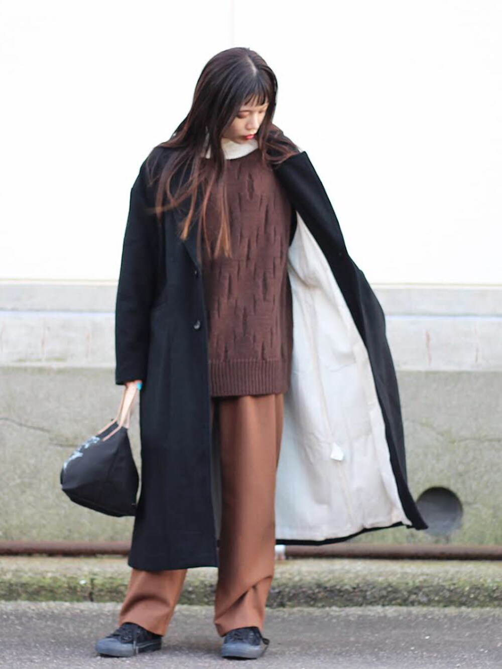 ブラック系のチェスターコート、ブラウン系のニット/セーター、ホワイト系のTシャツ/カットソーを着用したメンズの秋コーディネートの2枚目の写真