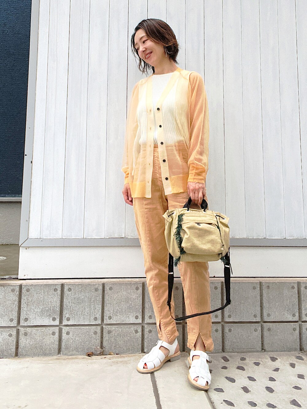オレンジ系のデニムパンツ、ホワイト系のサンダル、ベージュ系のカーディガン/ボレロを着用したレディースの秋コーディネートの2枚目の写真