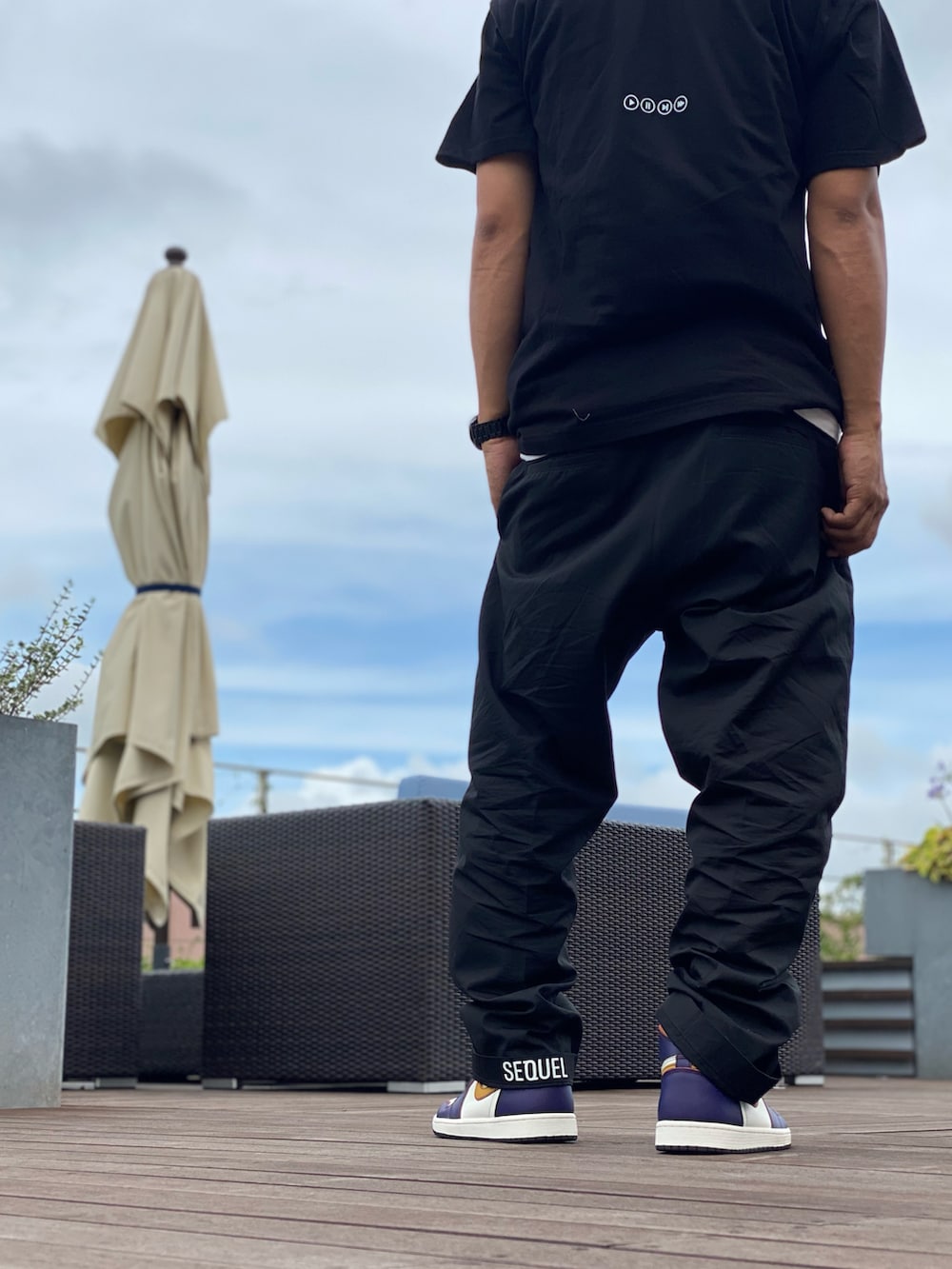 ブラック系のTシャツ/カットソー、ブラック系のチノパンツ、パープル系のスニーカーを着用したメンズの夏コーディネートの2枚目の写真