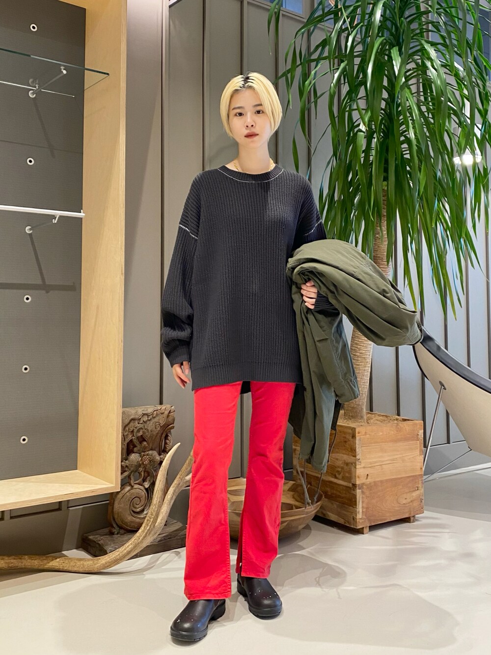 グリーン系のミリタリージャケット、レッド系のデニムパンツ、ブラック系のニット/セーターを着用したレディースの冬コーディネートの2枚目の写真