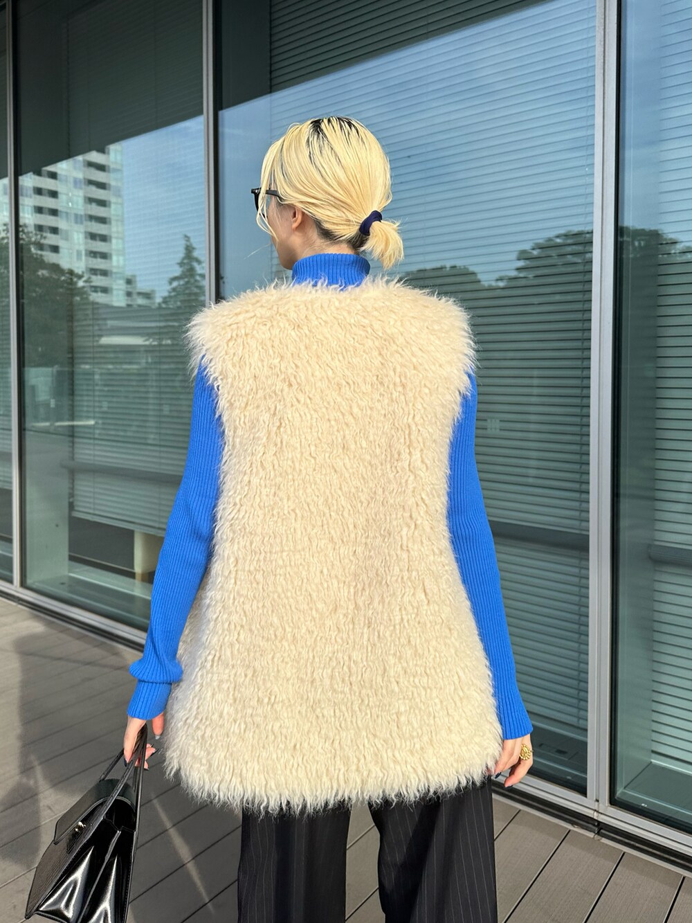 ブルー系のニット/セーター、ホワイト系のベスト、ブラック系のショルダーバッグを着用したレディースの秋コーディネートの3枚目の写真