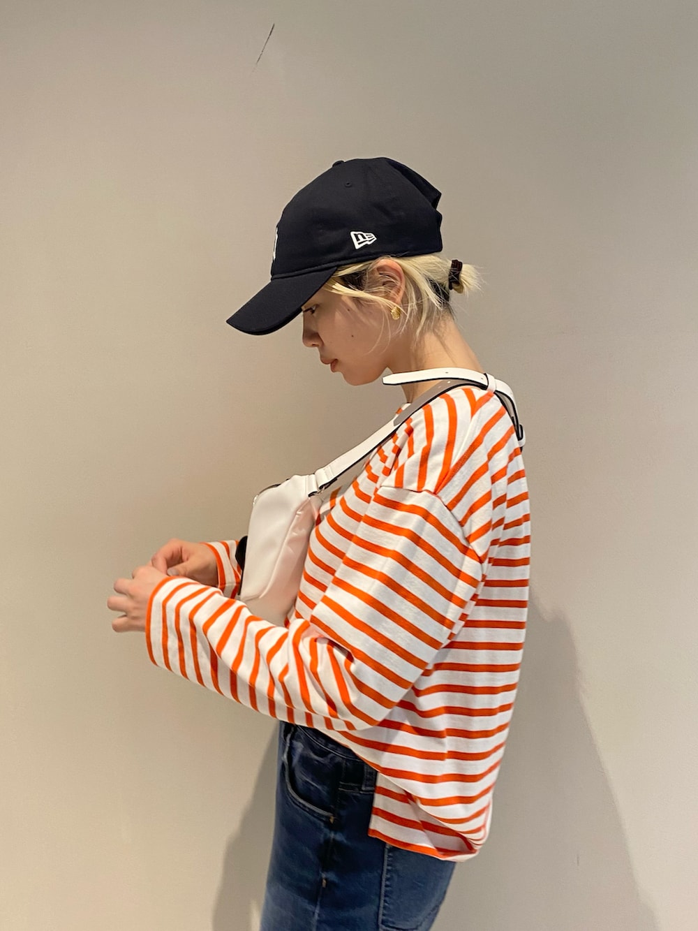 ホワイト系のボディバッグ/ウエストポーチ、オレンジ系のTシャツ/カットソー、ブルー系のデニムパンツを着用したレディースの冬コーディネートの4枚目の写真