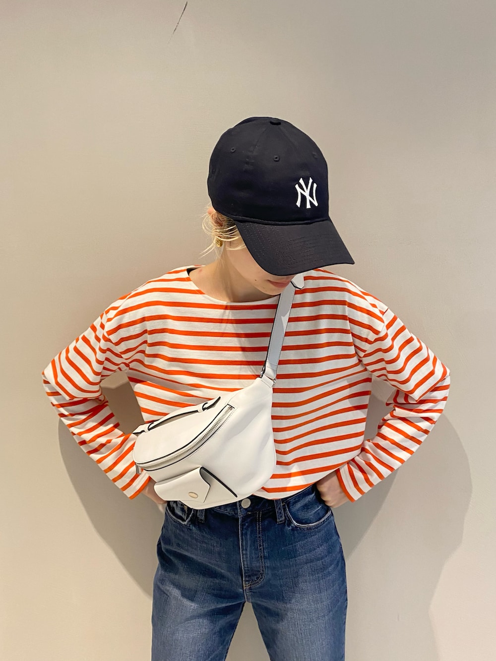 ホワイト系のボディバッグ/ウエストポーチ、オレンジ系のTシャツ/カットソー、ブルー系のデニムパンツを着用したレディースの冬コーディネートの3枚目の写真