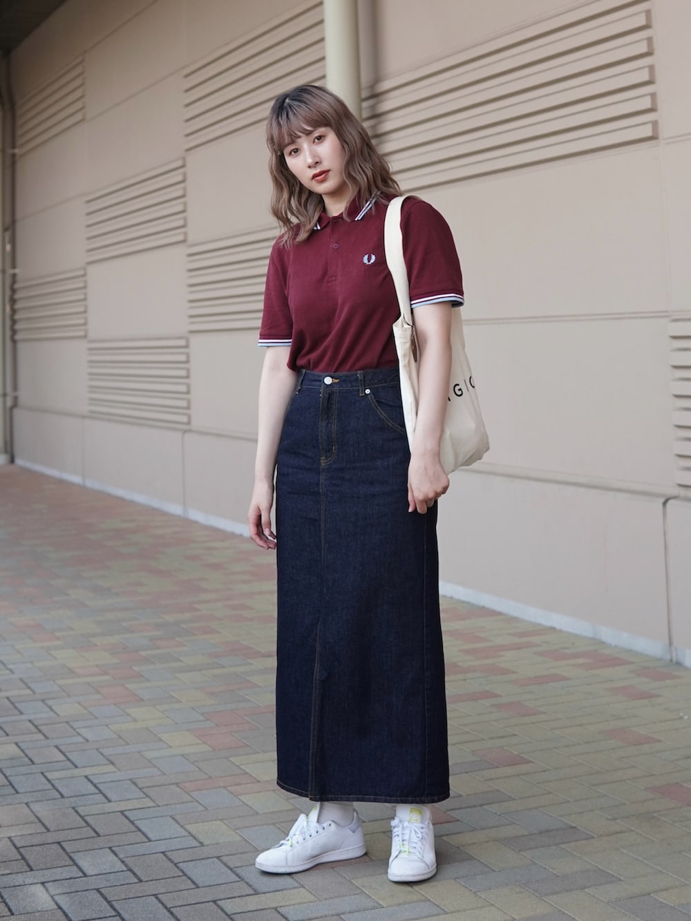 レッド系のポロシャツ、ブルー系のデニムスカート、ホワイト系のスニーカーを着用したレディースの夏コーディネートの2枚目の写真