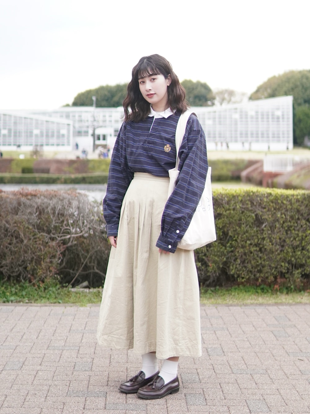 ベージュ系のスカート、ブラウン系のローファー、ブラック系のトートバッグを着用したレディースの春コーディネートの2枚目の写真