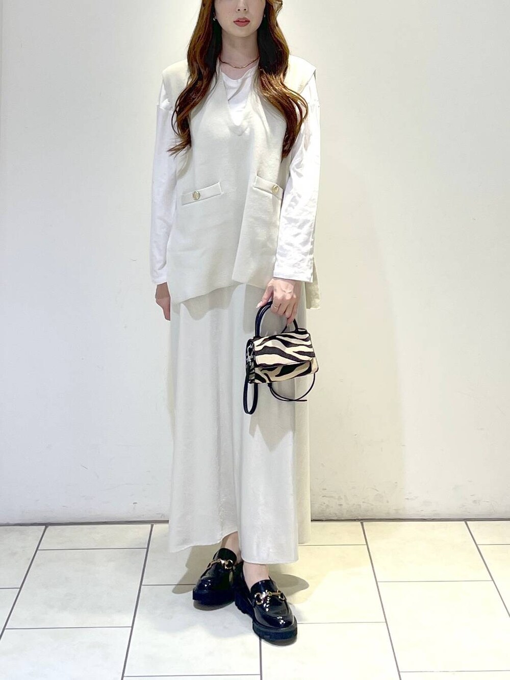 ブラック系のローファー、ベージュ系のベスト、ベージュ系のスカートを着用したレディースの春コーディネートの2枚目の写真