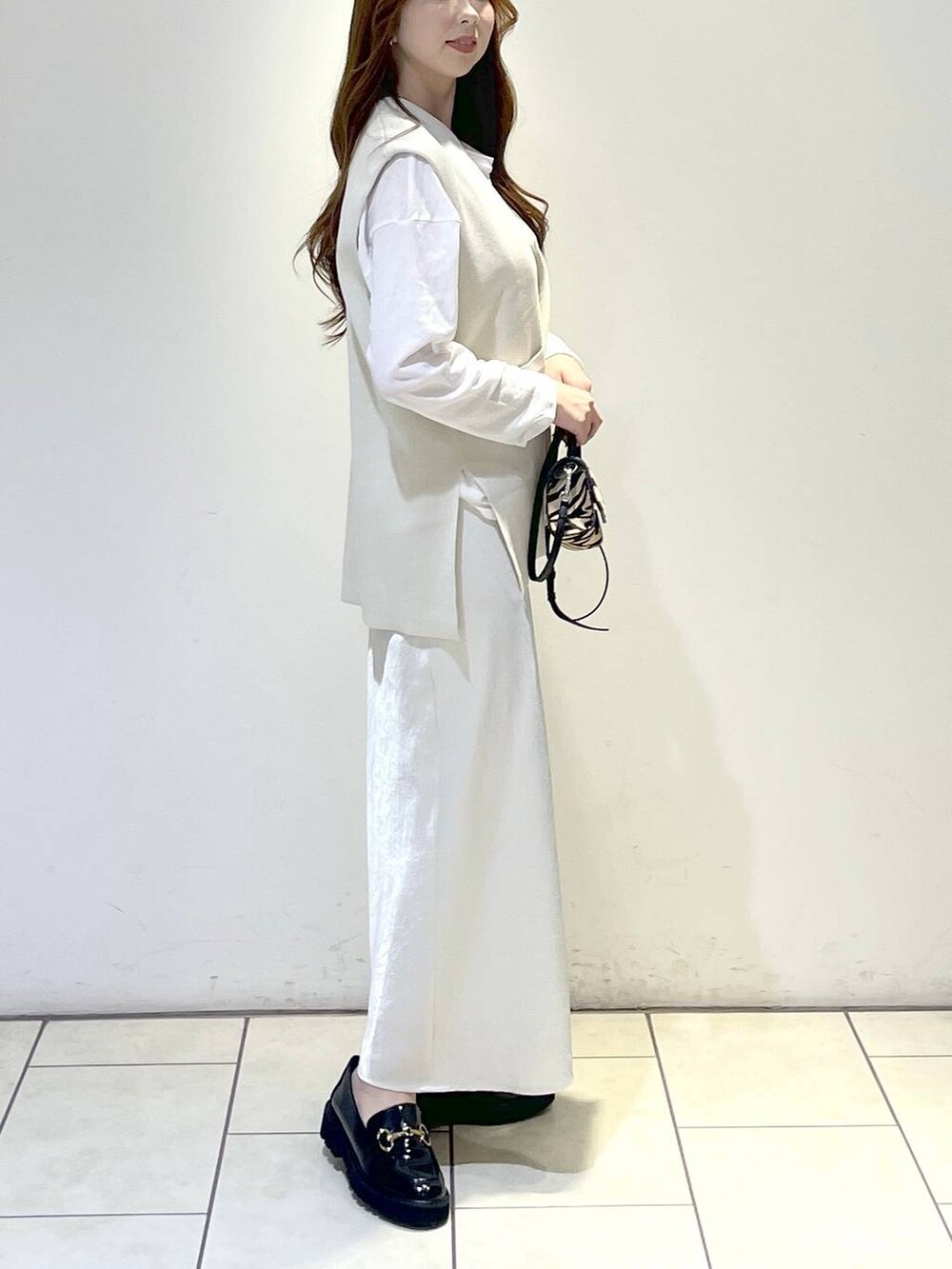 ブラック系のローファー、ベージュ系のベスト、ベージュ系のスカートを着用したレディースの春コーディネートの3枚目の写真