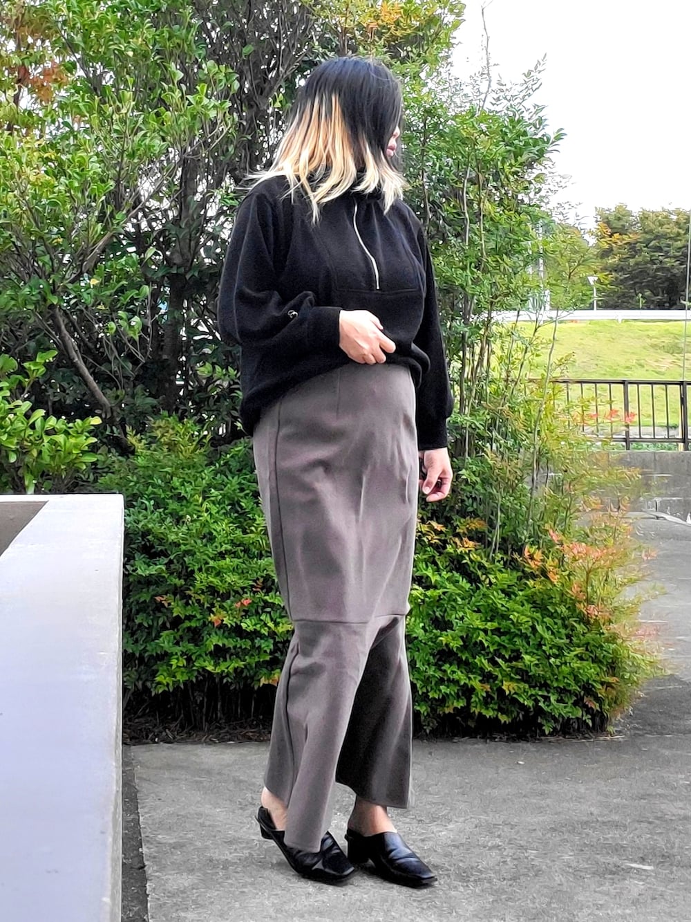 ブラック系のパンプス、グレー系のスカート、ブラック系のニット/セーターを着用したレディースの秋コーディネートの2枚目の写真