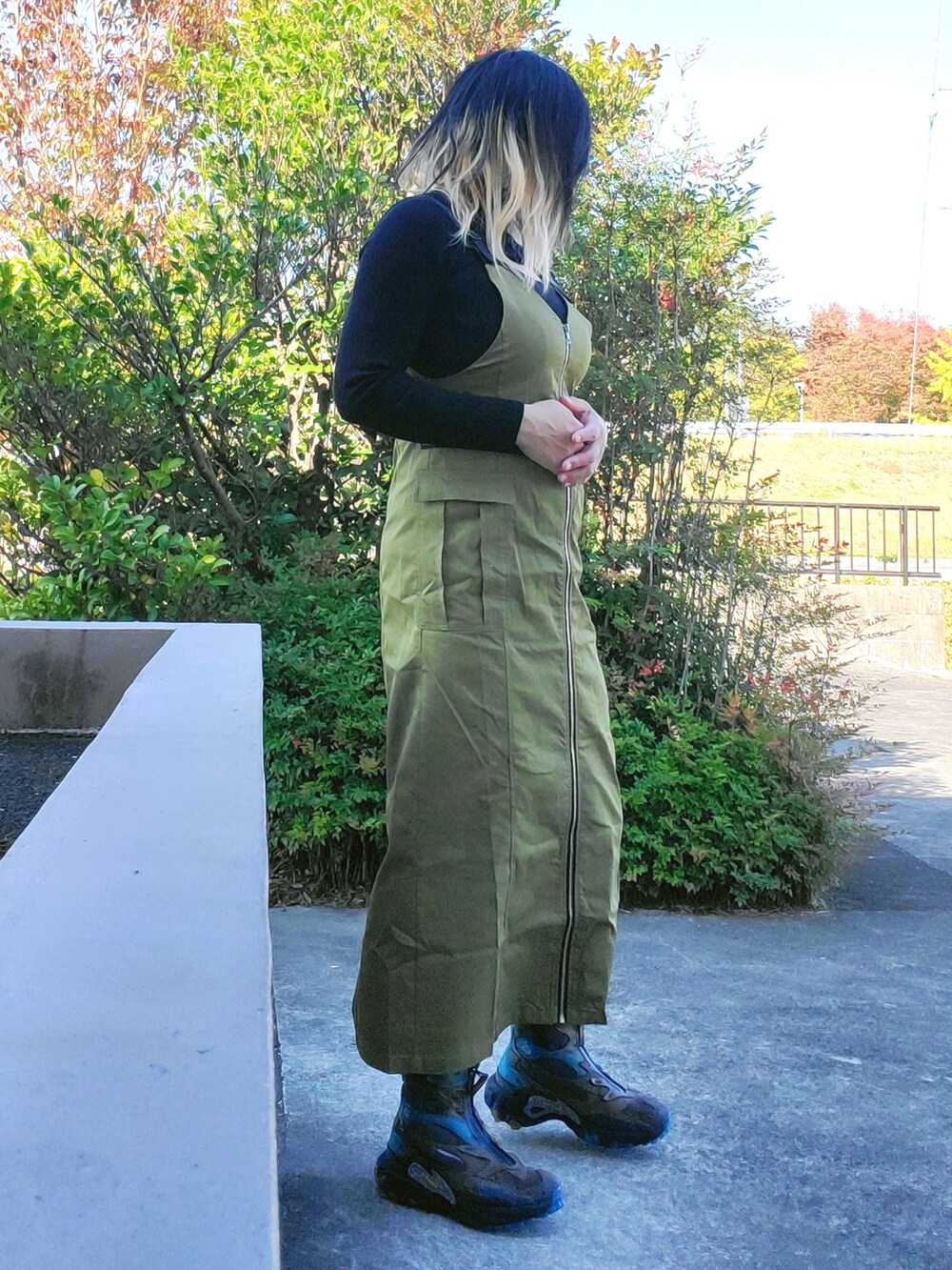 グリーン系のジャンパースカート、ブラック系のスニーカー、ブラック系のニット/セーターを着用したレディースの秋コーディネートの2枚目の写真