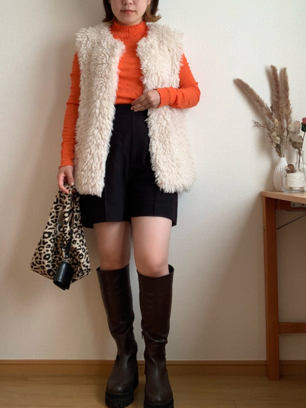 ブラック系のベスト、ブラウン系のブーツ、オレンジ系のTシャツ/カットソーを着用したレディースの秋コーディネートの2枚目の写真