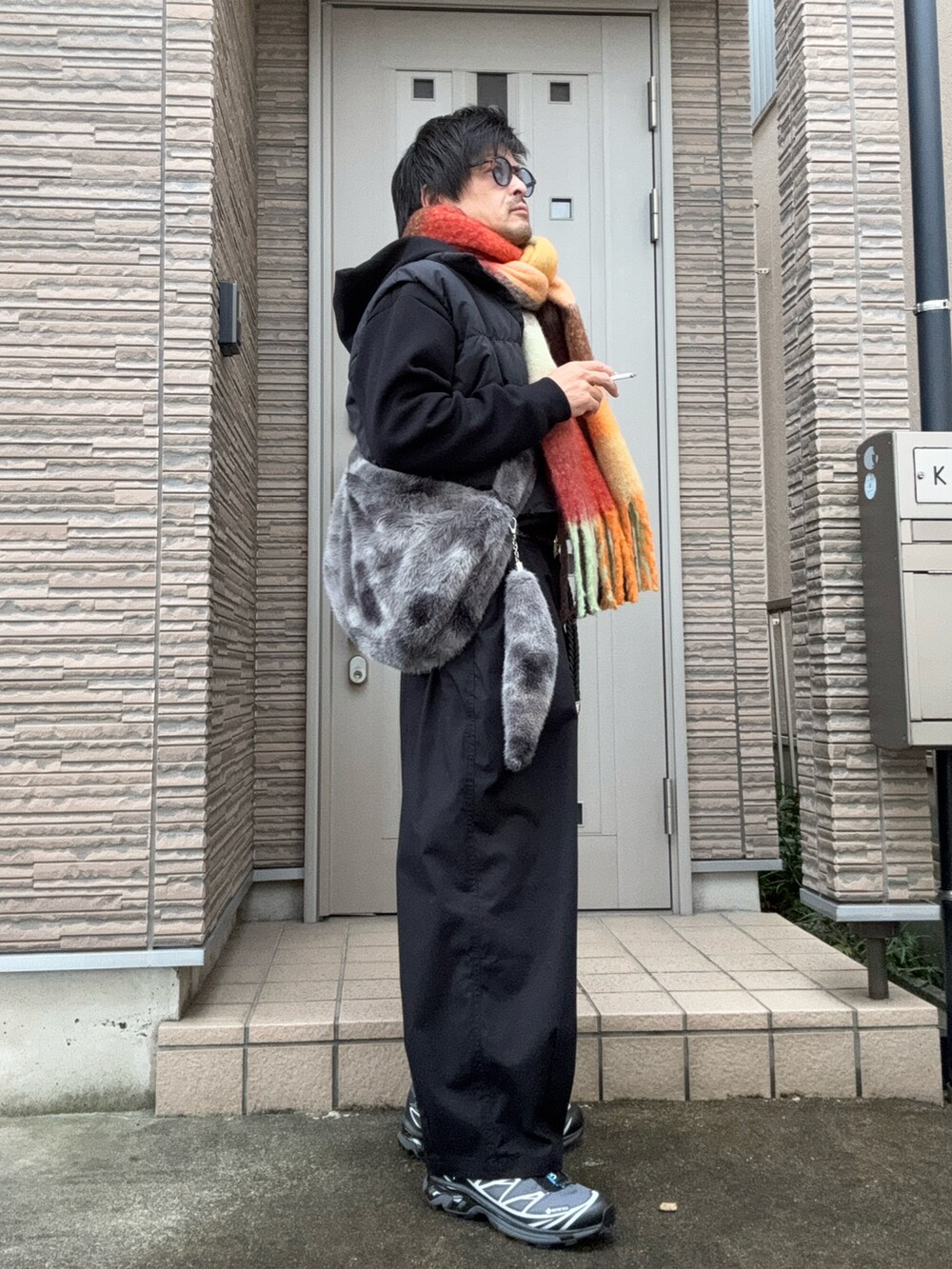 ブラック系のチノパンツ、ブラック系のスニーカー、グレー系のショルダーバッグを着用したメンズの冬コーディネートの2枚目の写真