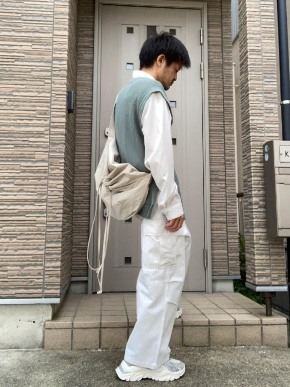 ホワイト系のカーゴパンツ、ベージュ系のスニーカー、グリーン系のベストを着用したメンズの春コーディネートの2枚目の写真