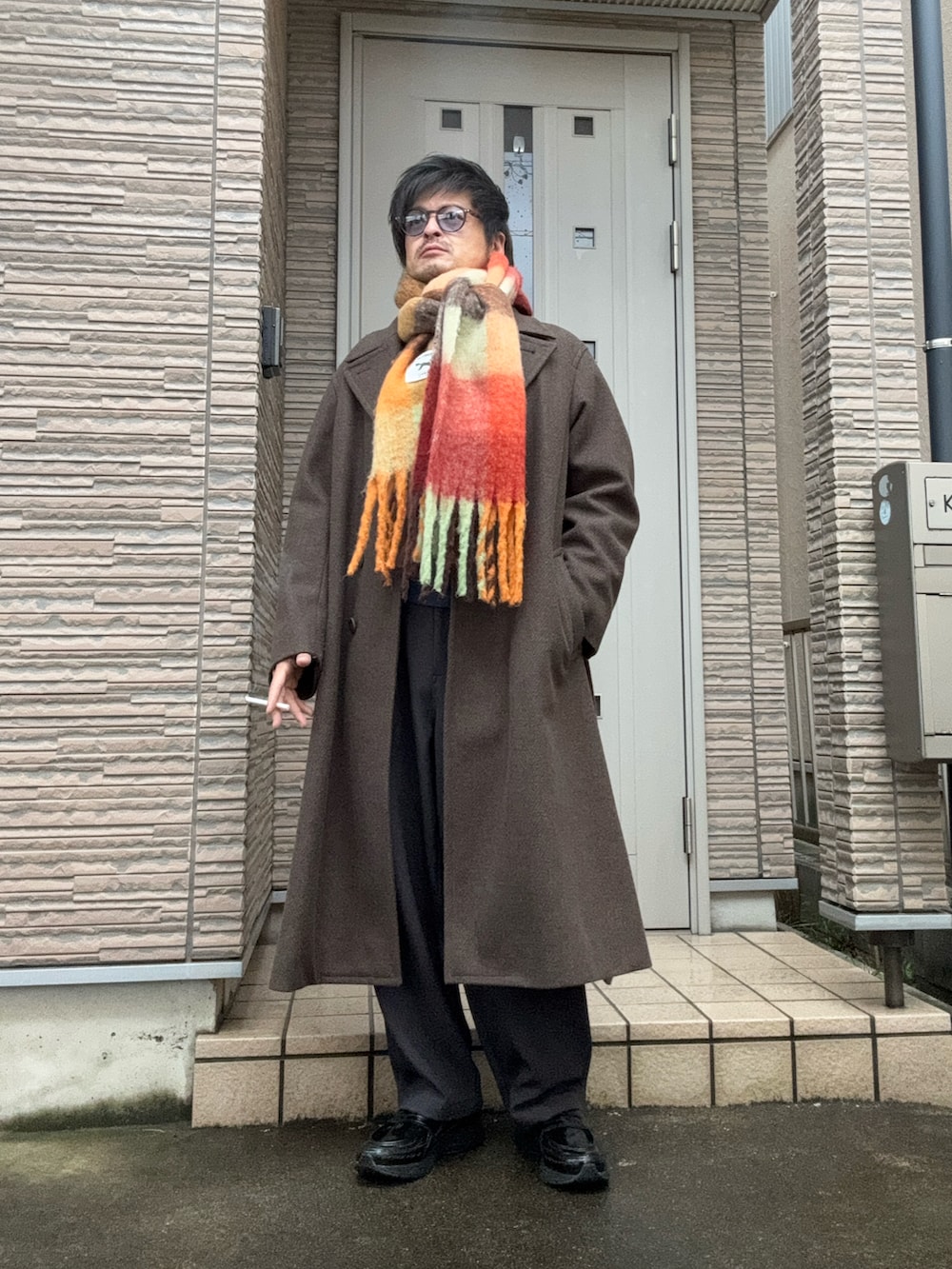 ブラウン系のチェスターコート、グレー系のその他パンツ、ブラック系のスニーカーを着用したメンズの冬コーディネートの2枚目の写真