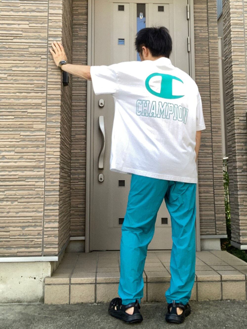 グリーン系のパンツ、ブラック系のサンダル、ホワイト系のTシャツ/カットソーを着用したメンズの夏コーディネートの2枚目の写真