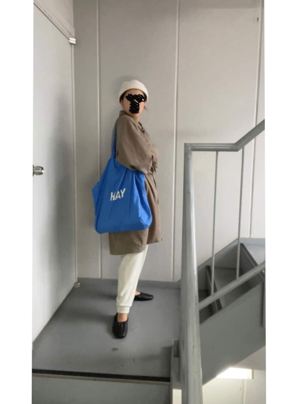 ブラウン系のステンカラーコート、ホワイト系のパンツ、ブルー系のトートバッグを着用したレディースの秋コーディネートの2枚目の写真