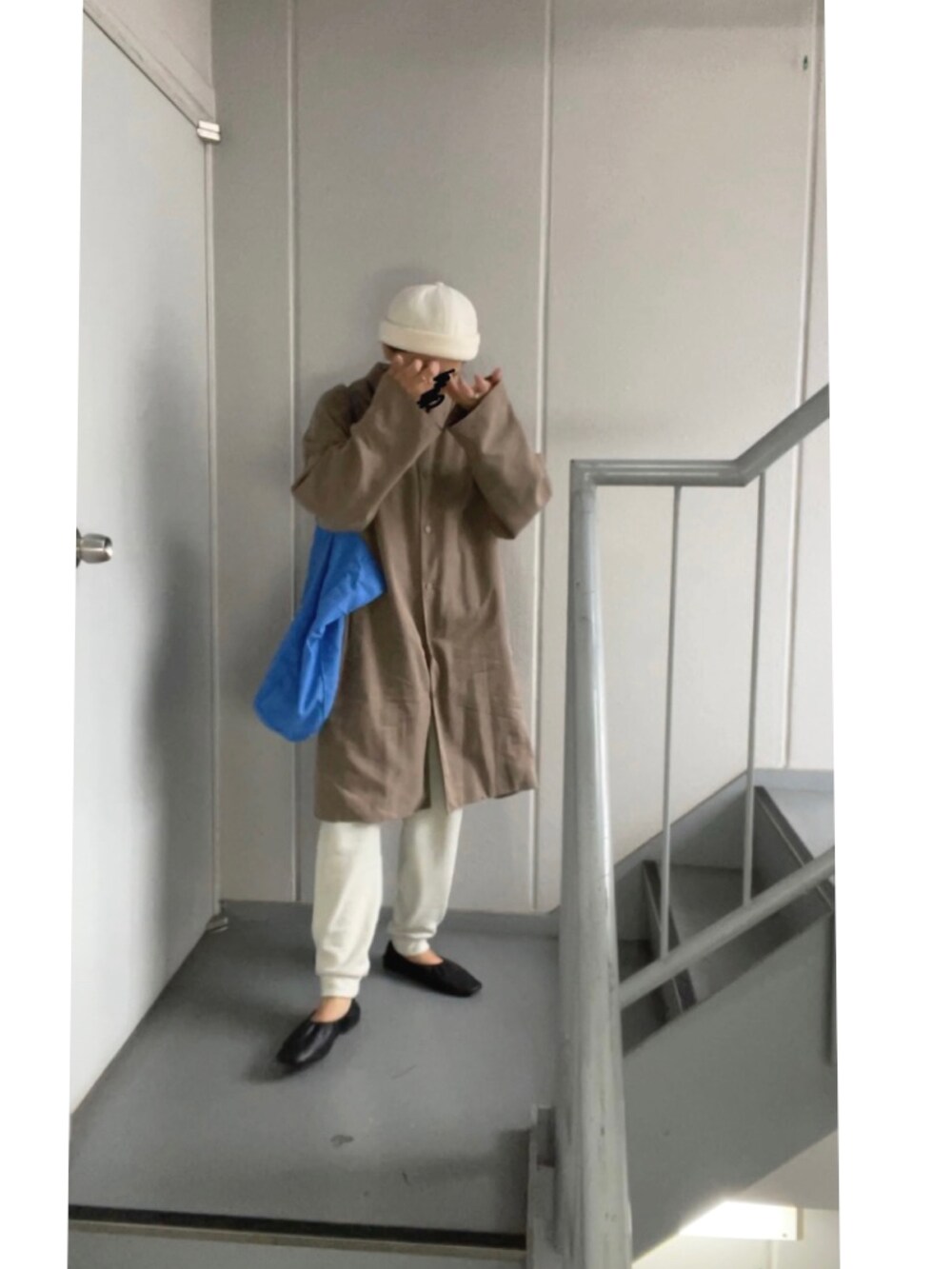 ブラウン系のステンカラーコート、ホワイト系のパンツ、ブルー系のトートバッグを着用したレディースの秋コーディネートの4枚目の写真