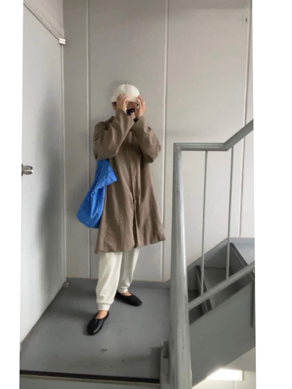 ブラウン系のステンカラーコート、ホワイト系のパンツ、ブルー系のトートバッグを着用したレディースの秋コーディネートの3枚目の写真