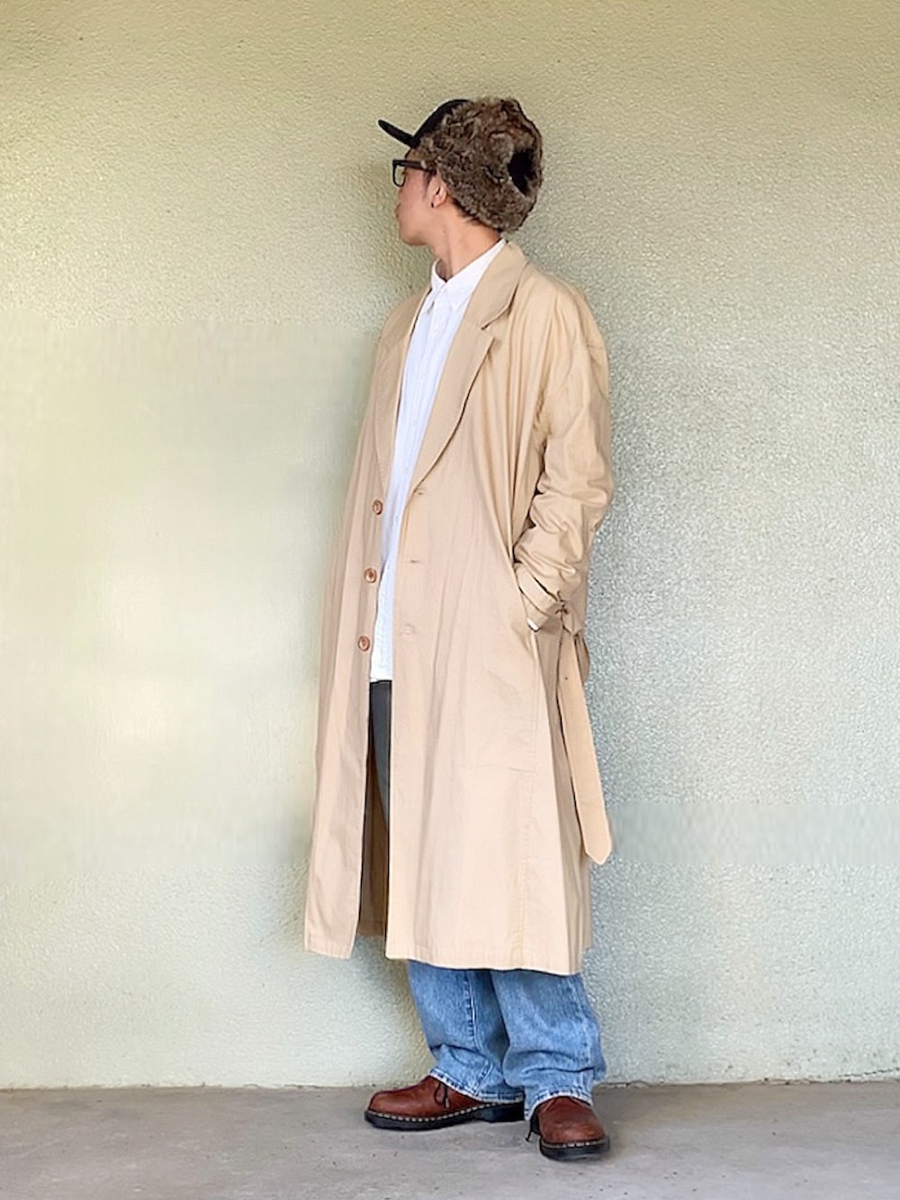 ブラウン系のベスト、ベージュ系のトレンチコート、ブルー系のデニムパンツを着用したメンズの秋コーディネートの2枚目の写真