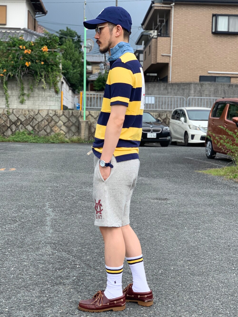 イエロー系のポロシャツ、グレー系のパンツ、レッド系のモカシン/デッキシューズを着用したメンズの夏コーディネートの2枚目の写真