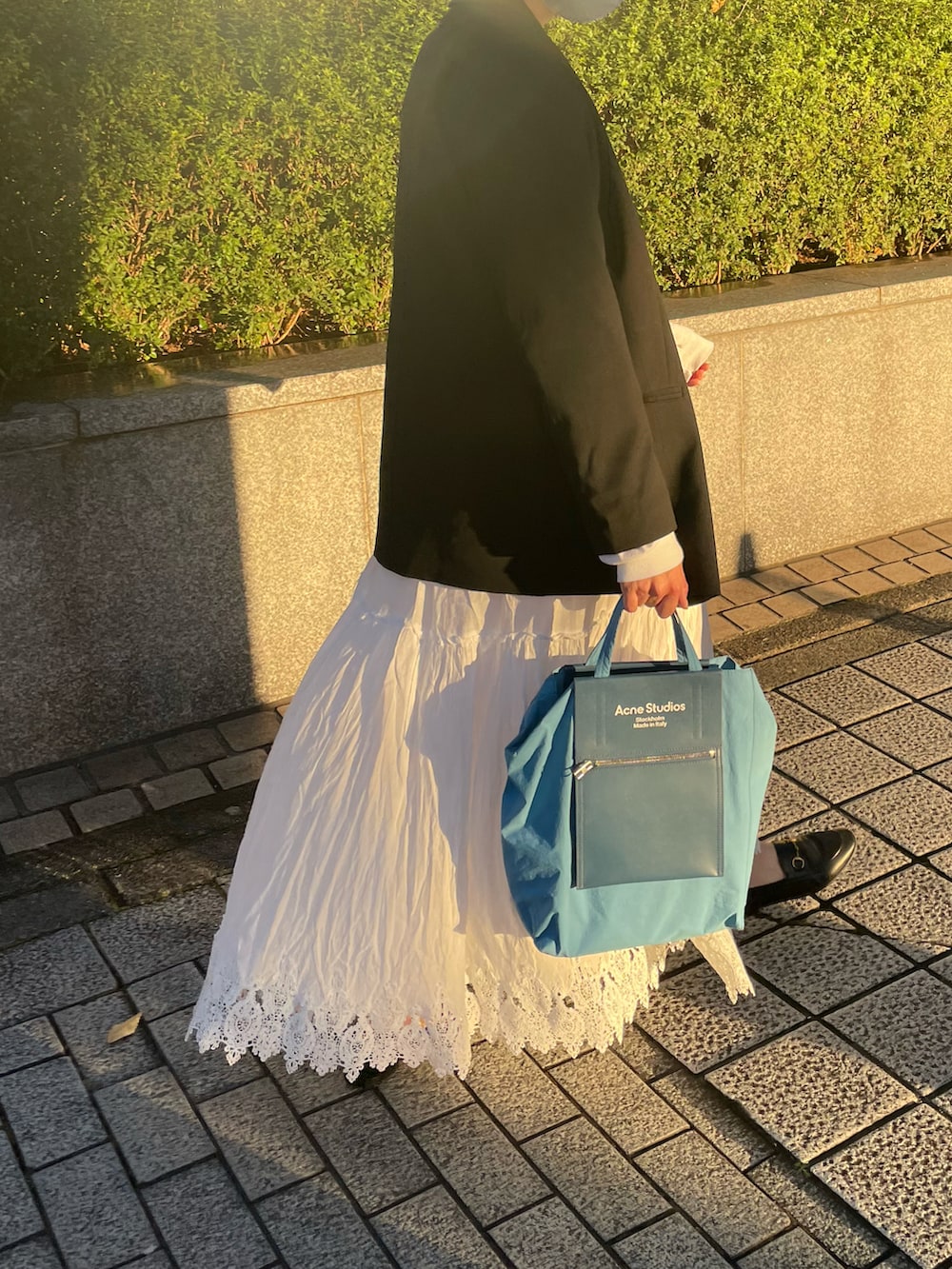 ブラック系のテーラードジャケット、ホワイト系のスカート、ブラック系のトートバッグを着用したレディースの秋コーディネートの2枚目の写真