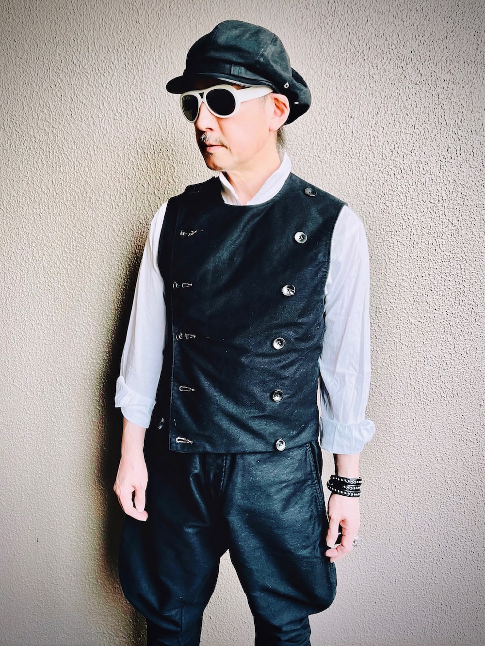 ブラック系のベスト、ブラック系のチノパンツ、ブラック系のブーツを着用したメンズの春コーディネートの2枚目の写真