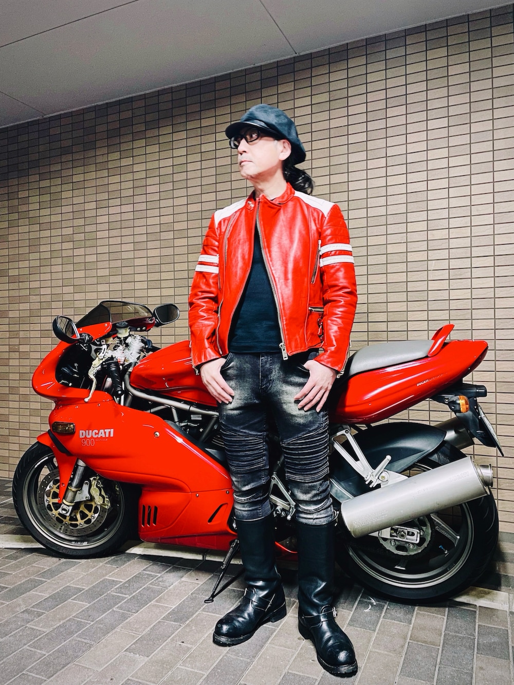 レッド系のライダースジャケット、ブラック系のデニムパンツ、ブラック系のブーツを着用したメンズの冬コーディネートの2枚目の写真