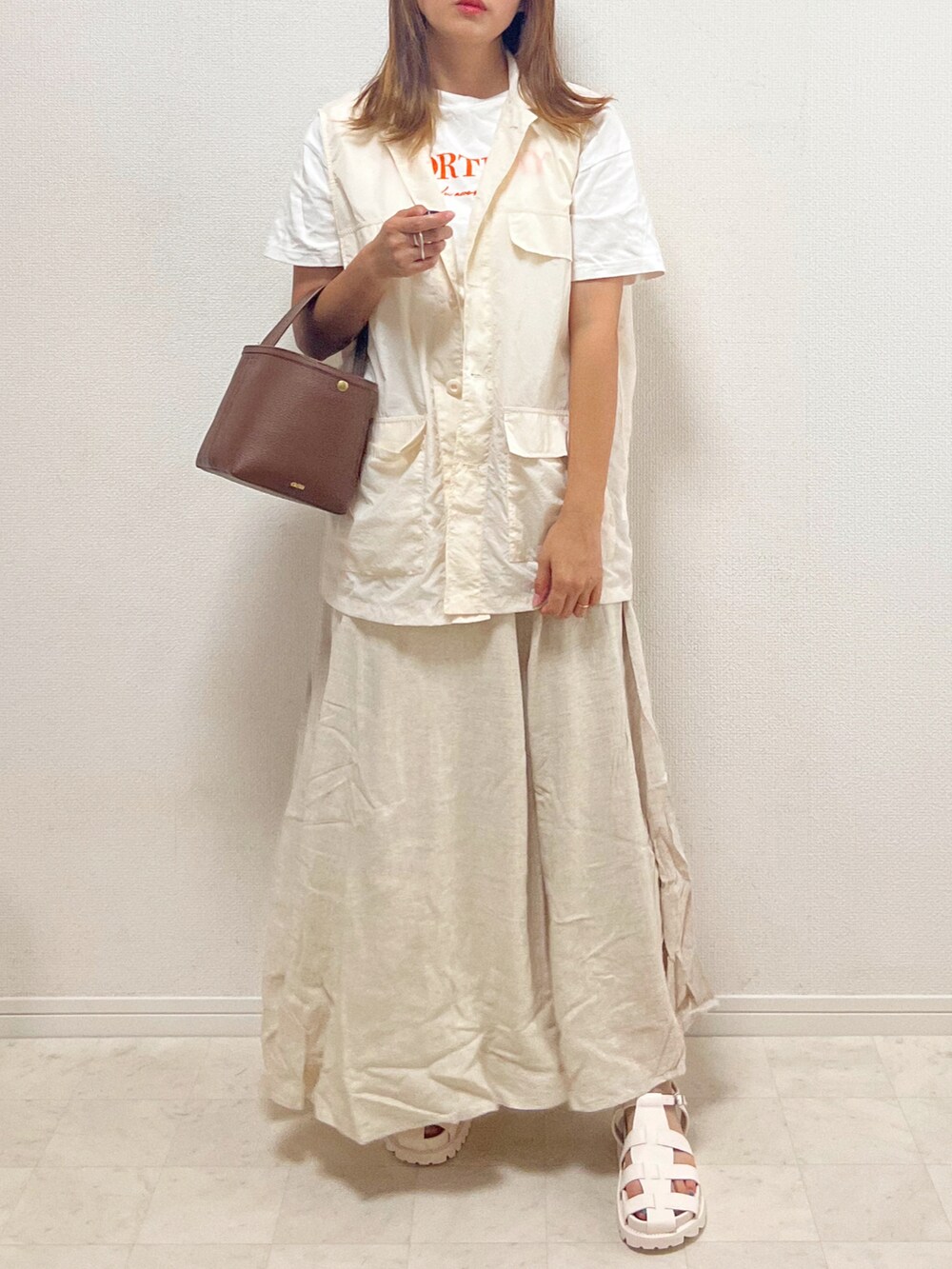 ベージュ系のスカート、ホワイト系のベスト、ブラウン系のバッグを着用したレディースの夏コーディネートの2枚目の写真