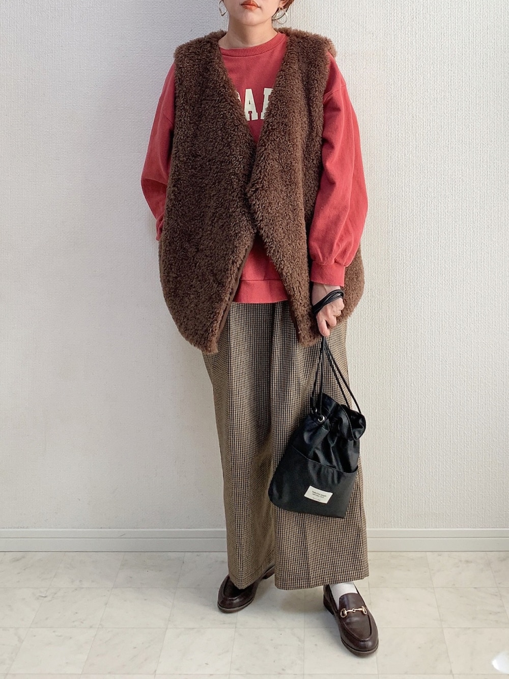 ブラウン系のベスト、ブラック系のショルダーバッグ、ブラウン系のパンツを着用したレディースの冬コーディネートの2枚目の写真