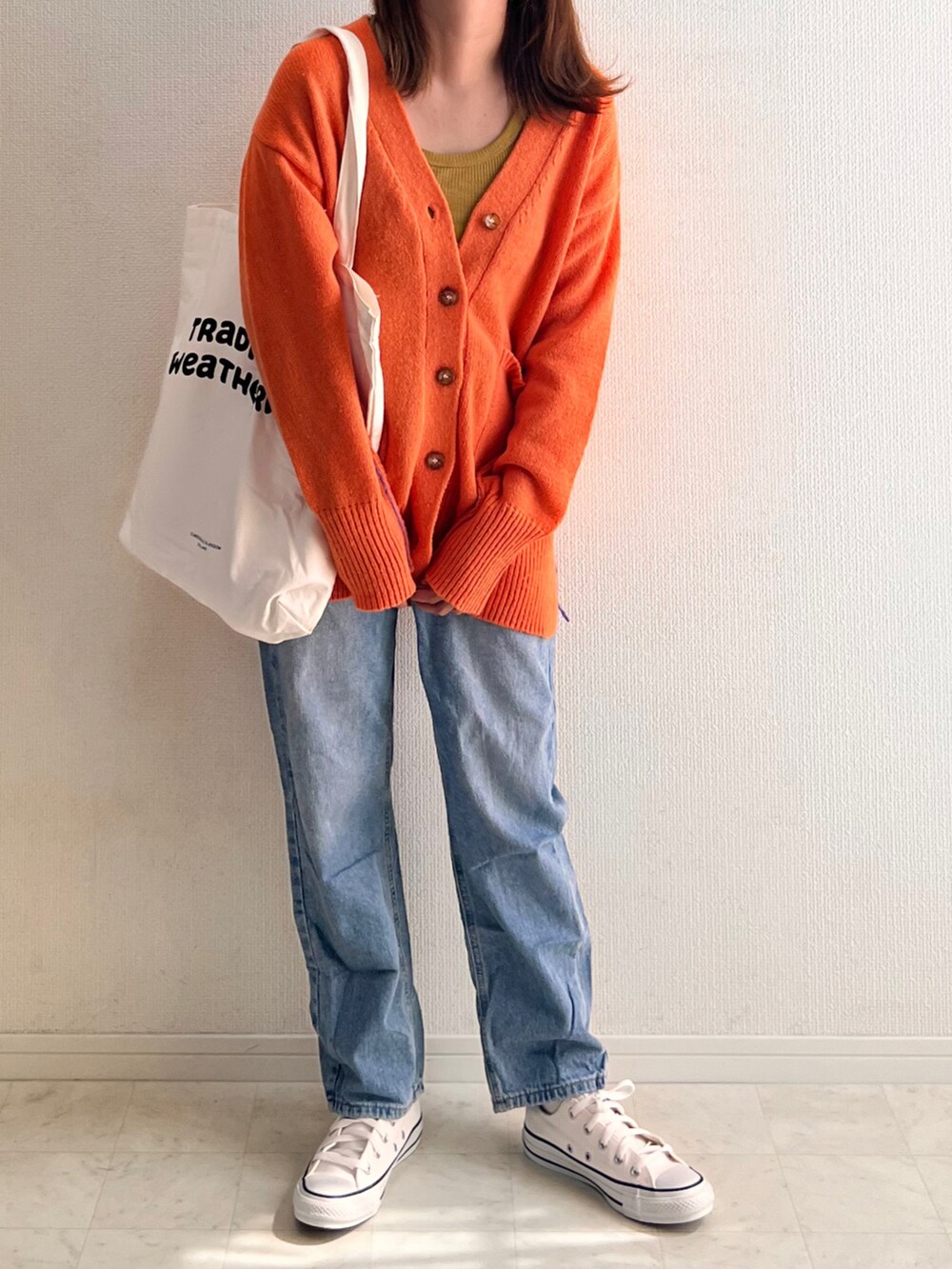 オレンジ系のカーディガン/ボレロ、ホワイト系のトートバッグ、ブルー系のデニムパンツを着用したレディースの秋コーディネートの3枚目の写真