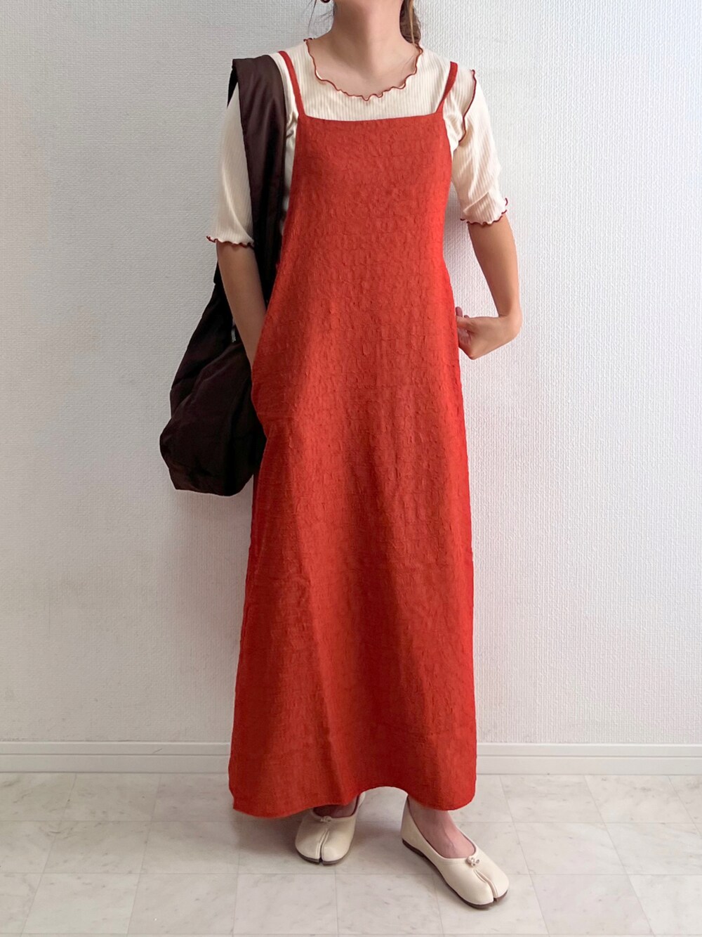 オレンジ系のワンピース、ホワイト系のTシャツ/カットソー、ブラウン系のショルダーバッグを着用したレディースの夏コーディネートの2枚目の写真