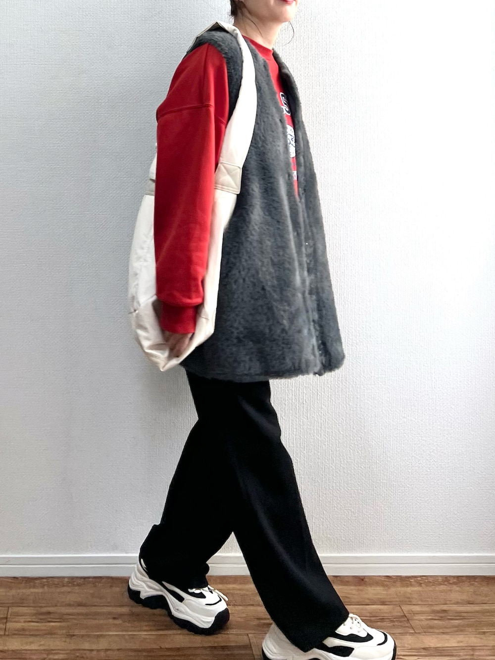 グレー系のベスト、ベージュ系のショルダーバッグ、レッド系のスウェットを着用したレディースの冬コーディネートの3枚目の写真