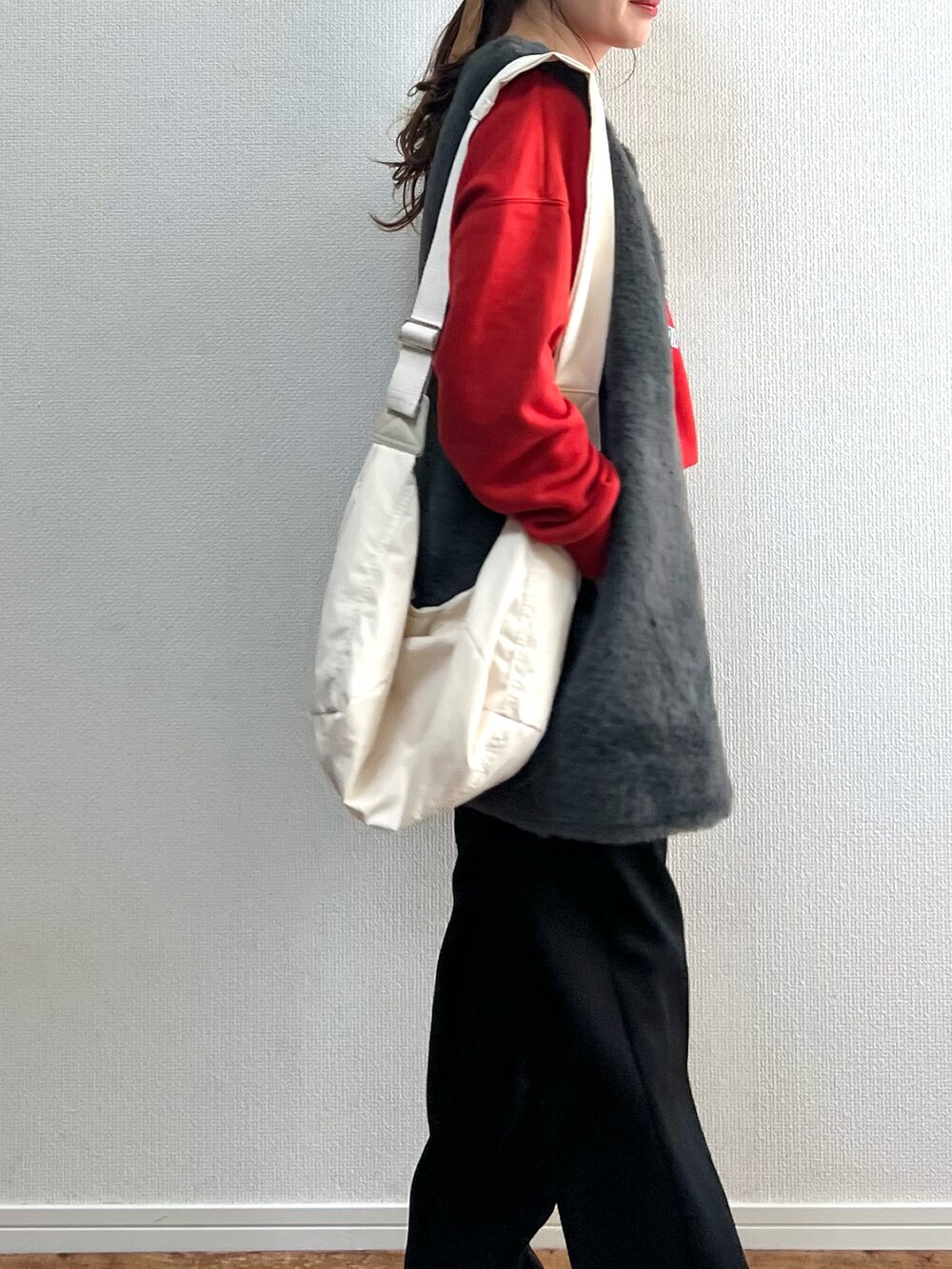 グレー系のベスト、ベージュ系のショルダーバッグ、レッド系のスウェットを着用したレディースの冬コーディネートの2枚目の写真