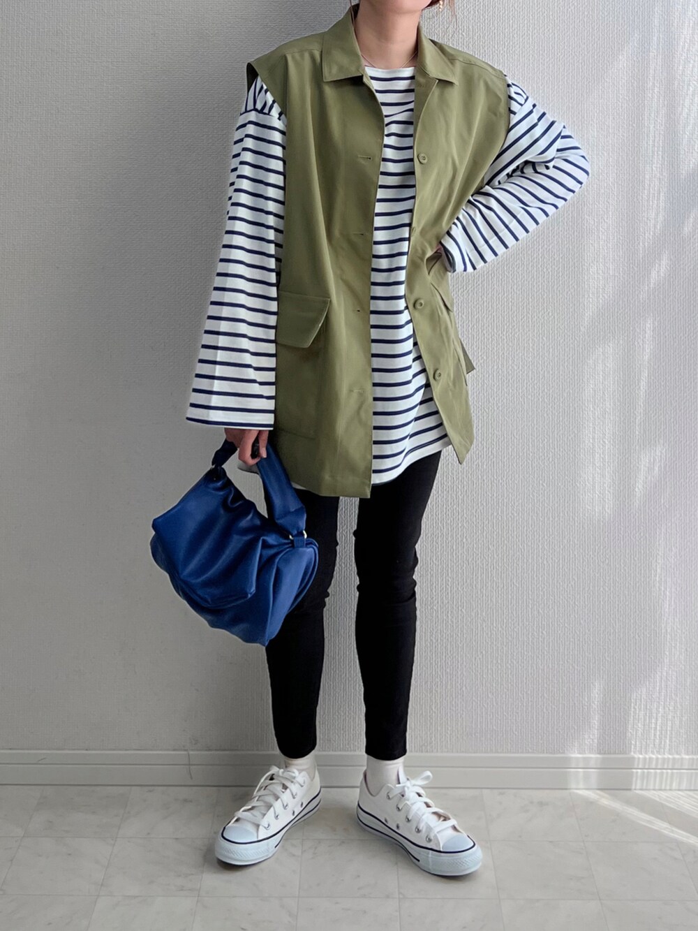 グリーン系のベスト、ブルー系のトップス、ブルー系のショルダーバッグを着用したレディースの春コーディネートの2枚目の写真