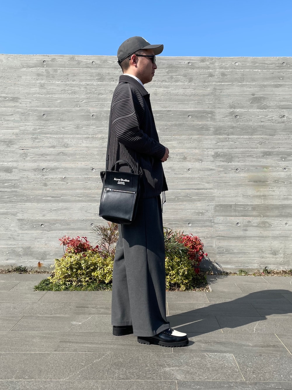 グレー系のブルゾン、ブラック系のトートバッグ、グレー系のスラックスを着用したメンズの春コーディネートの3枚目の写真