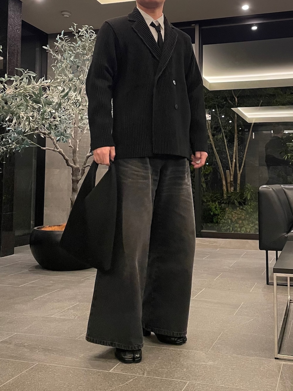 ブラック系のデニムパンツ、ブラック系のトートバッグ、ブラック系のブーツを着用したメンズの春コーディネートの5枚目の写真