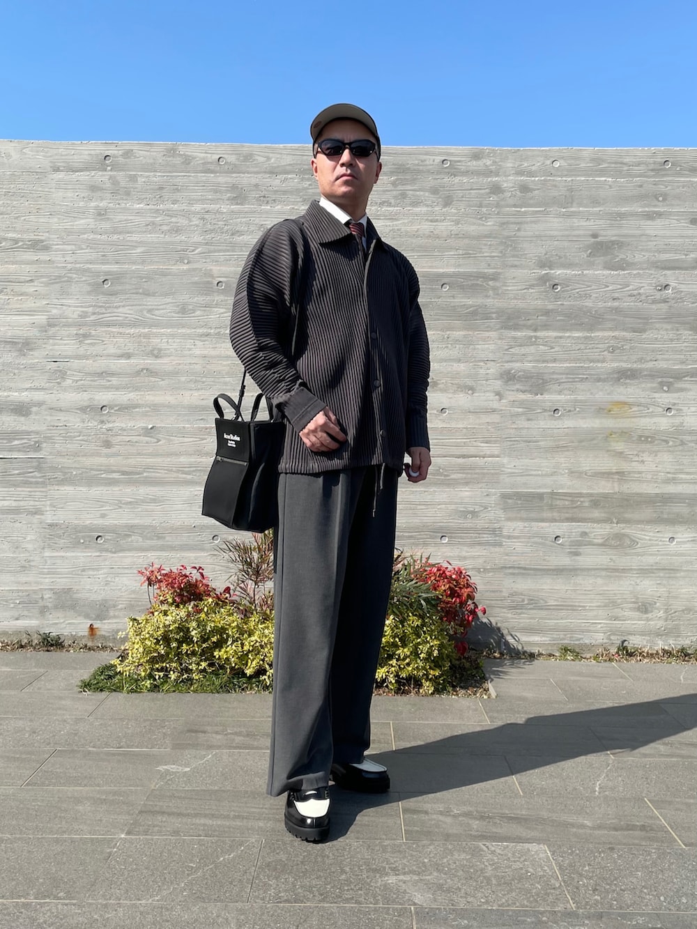 グレー系のブルゾン、ブラック系のトートバッグ、グレー系のスラックスを着用したメンズの春コーディネートの4枚目の写真