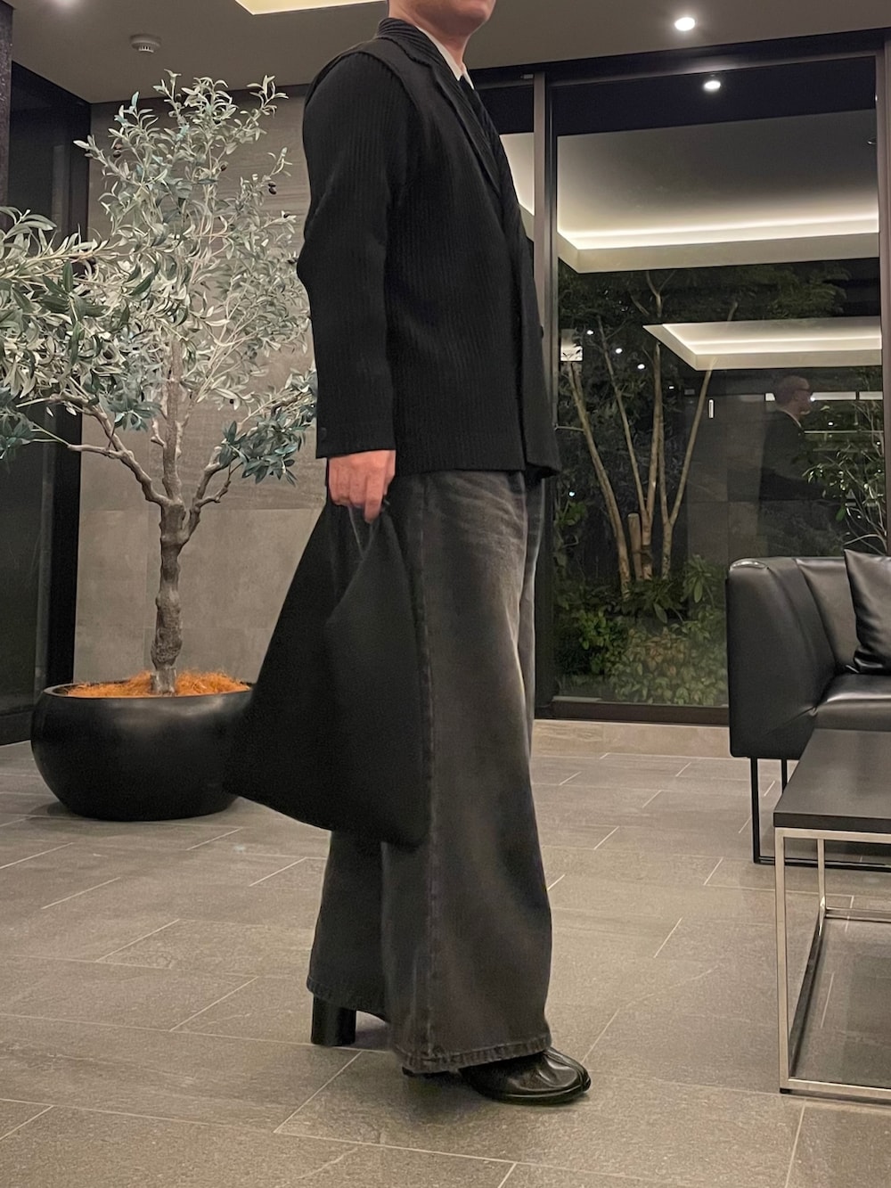 ブラック系のデニムパンツ、ブラック系のトートバッグ、ブラック系のブーツを着用したメンズの春コーディネートの3枚目の写真