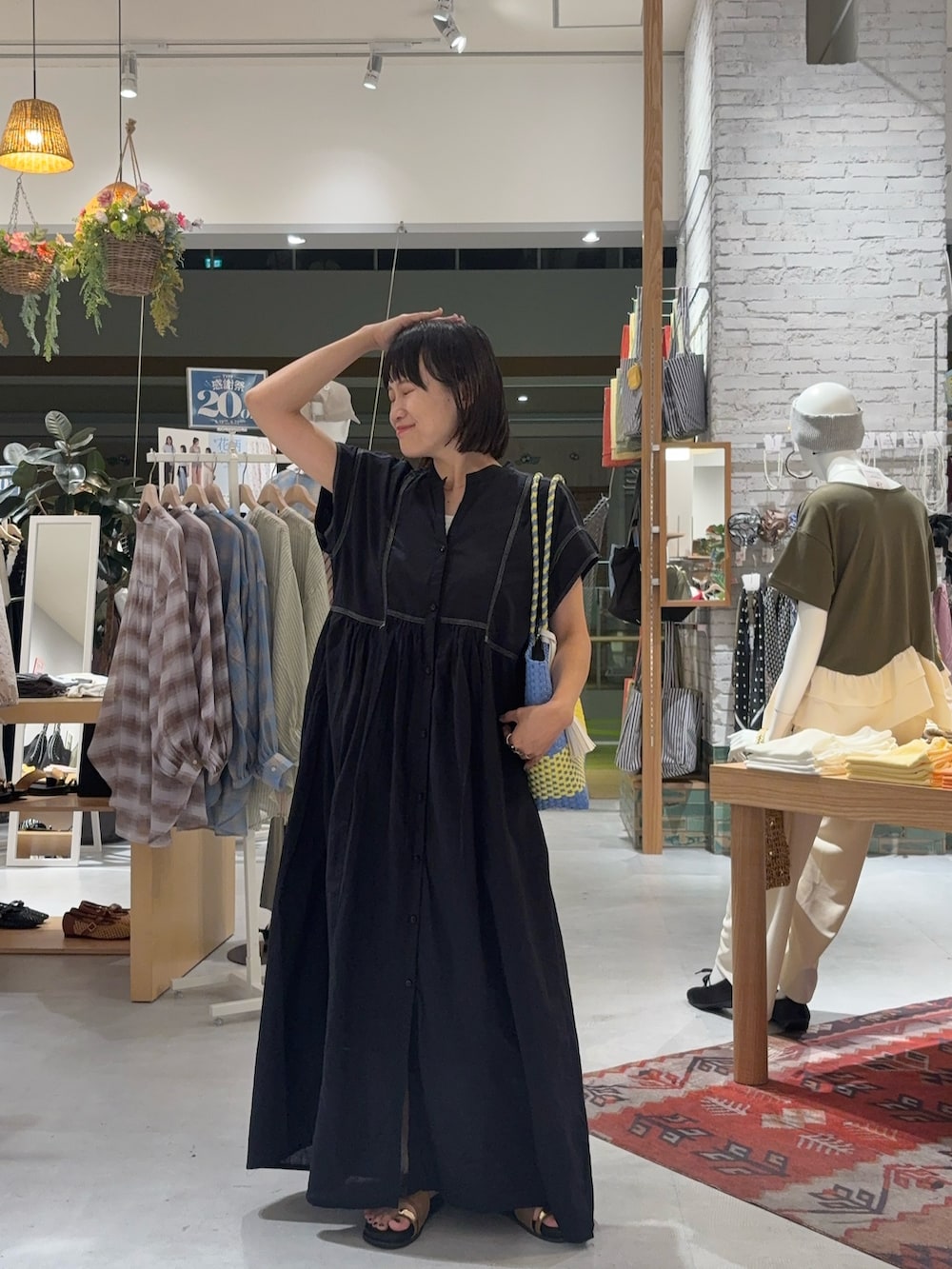 ブラック系のワンピース、イエロー系のサンダル、ブルー系のトートバッグを着用したレディースの夏コーディネートの2枚目の写真