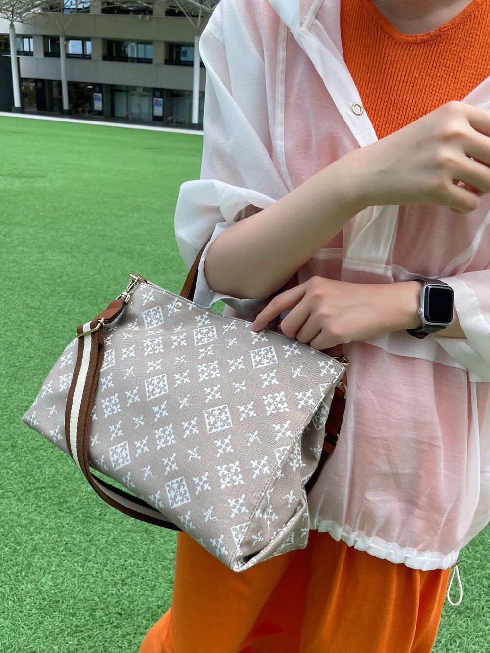 オレンジ系のワンピース、ベージュ系のショルダーバッグ、ホワイト系のパーカーを着用したレディースの夏コーディネートの2枚目の写真