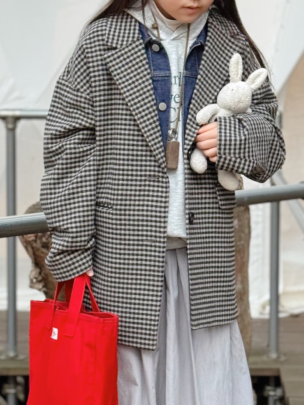 ブルー系のデニムジャケット、レッド系のトートバッグ、ブラック系のチェスターコートを着用したキッズの冬コーディネートの2枚目の写真
