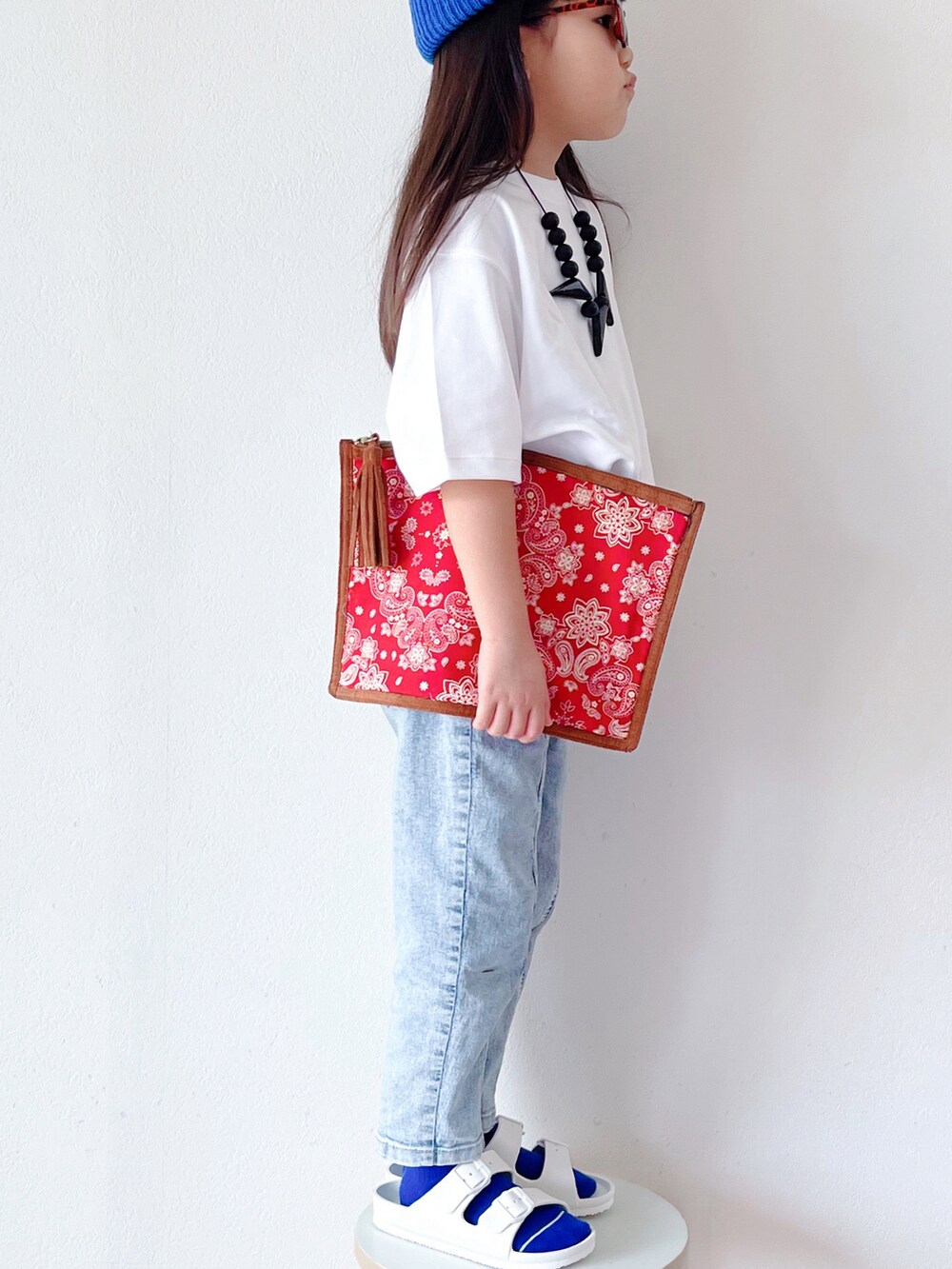 ホワイト系のTシャツ/カットソー、ブルー系のデニムパンツ、レッド系のクラッチバッグを着用したキッズの春コーディネートの2枚目の写真
