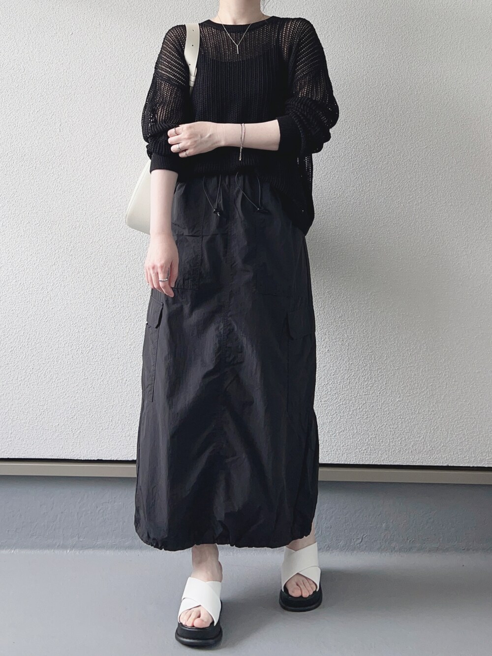 ブラック系のニット/セーター、ブラック系のスカート、ホワイト系のバッグを着用したレディースの春コーディネートの2枚目の写真