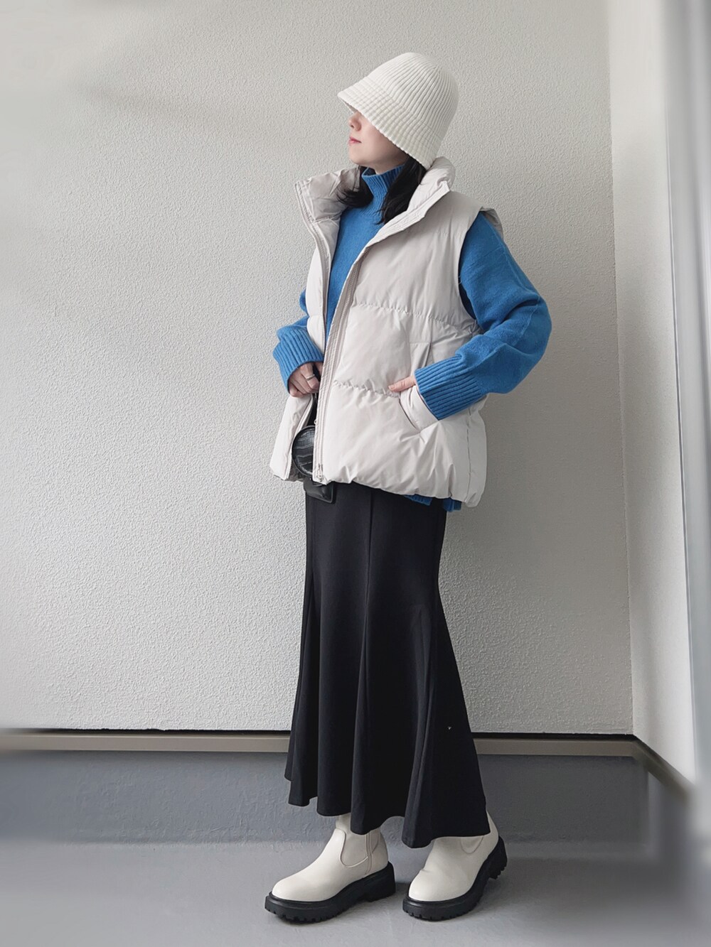 ホワイト系のダウンベスト、ブルー系のニット/セーター、ブラック系のスカートを着用したレディースの秋コーディネートの2枚目の写真