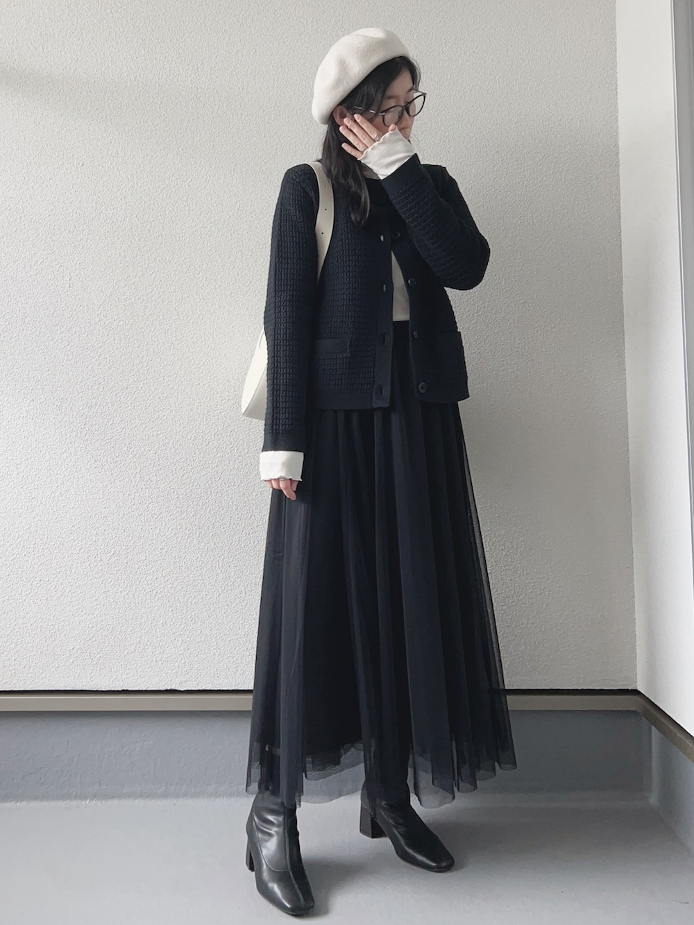 ブラック系のスカート、ブラック系のカーディガン/ボレロ、ホワイト系のバッグを着用したレディースの冬コーディネートの2枚目の写真